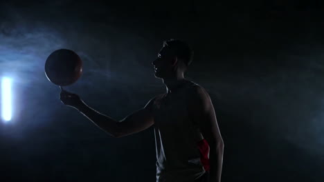 Hooded-basketball-player-spinning-the-ball-at-night-in-an-empty-car-park,-in-slow-motion